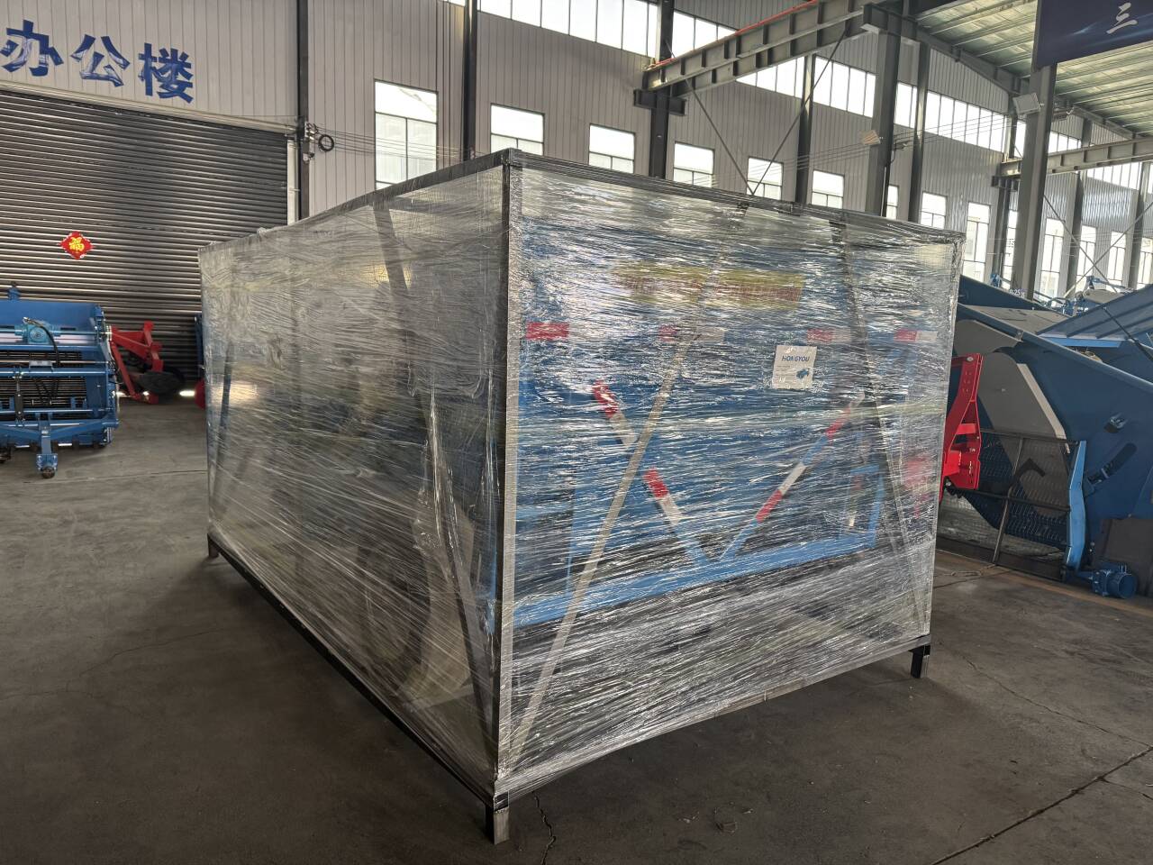 Large machine enclosed in a heavy steel-frame crate and stretch-wrapped before loading.