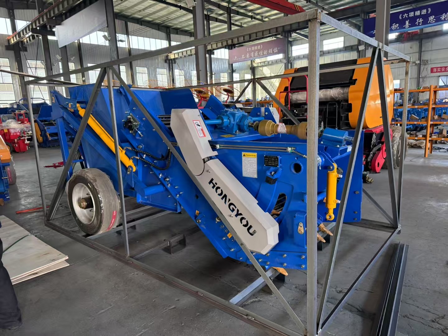Blue potato harvester positioned inside a welded steel export frame before final wrapping.