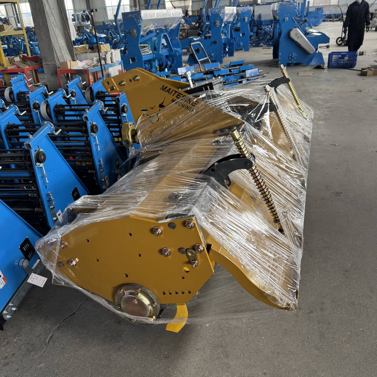 Yellow haulm topper wrapped for export beside finished potato harvesters on the assembly floor.