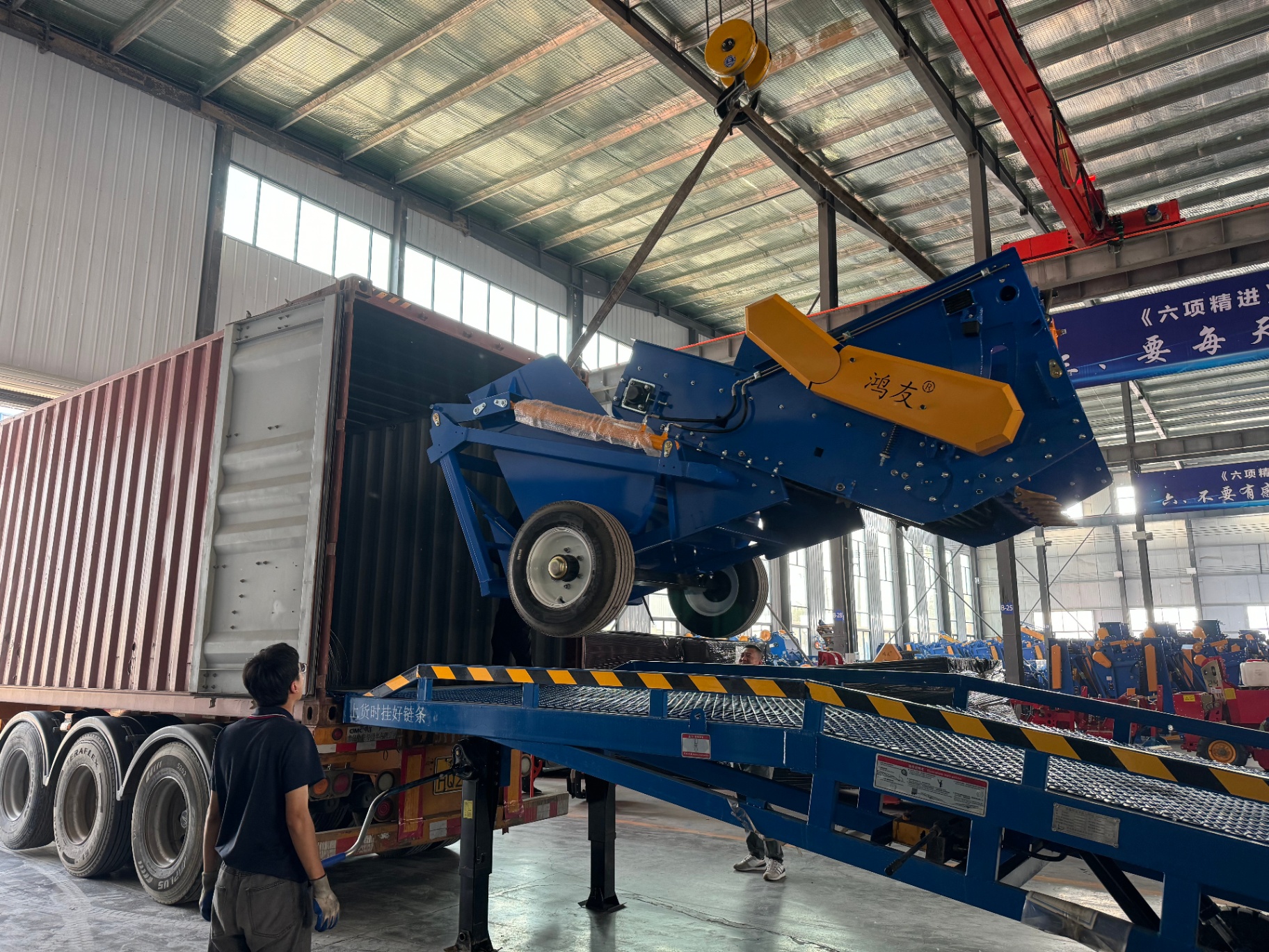 Stone picker craned into a 40HQ container via dock ramp — Hongyou (鸿友) brand visible on machine cowl.