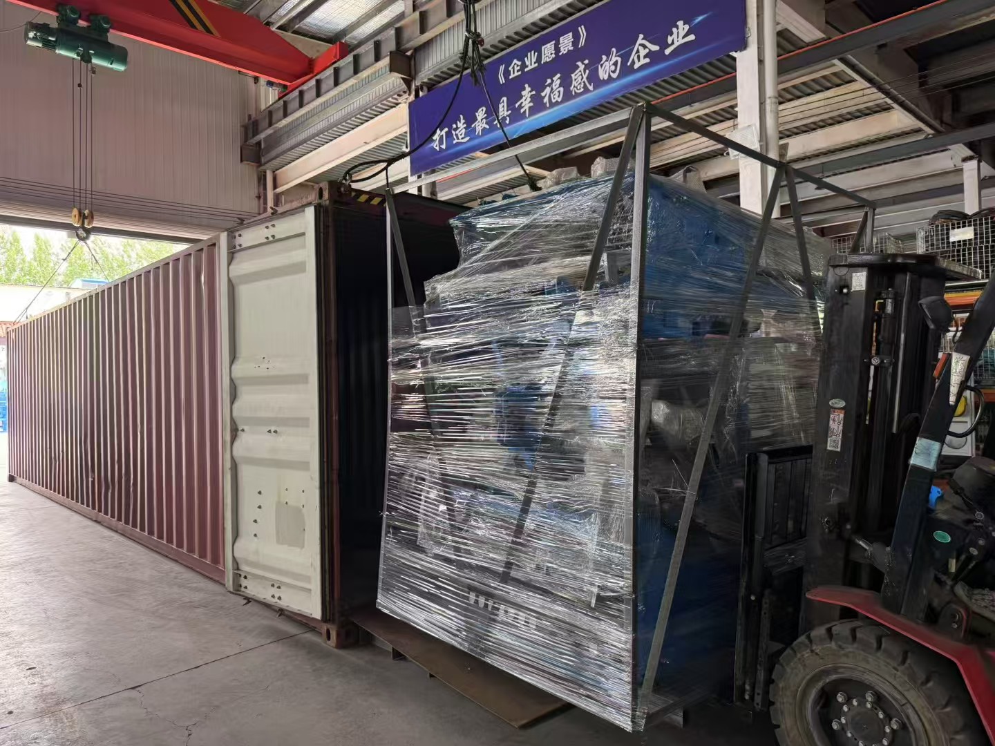 Shrink-wrapped steel-frame crate being forked into a 40HQ container.